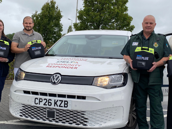 Mae cynrychiolwyr o Llesiant Delta a Save a Life Cymru yn sefyll wrth ymyl cerbyd Ymateb Cymunedol