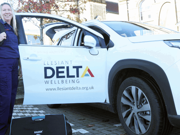Swyddog Ymateb yn sefyll wrth ymyl car Llesiant Delta