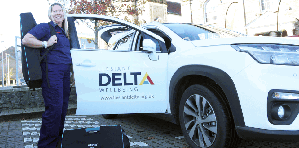 Swyddog Ymateb yn sefyll wrth ymyl car Llesiant Delta