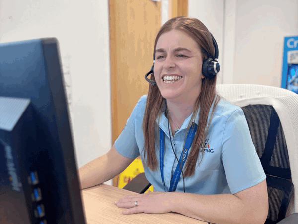 Cynghorydd Llesiant Delta yn eistedd wrth ddesg yn ateb galwadau brys